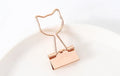 Gold metal paper clip with a long tail, showing decorative flamingo, love, cloud, cat, cactus, and bow motif options.
