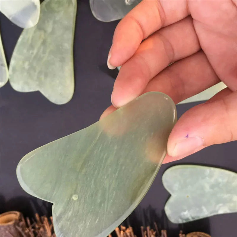 Flat natural jade gua sha stone for facial massage in green colour on white background