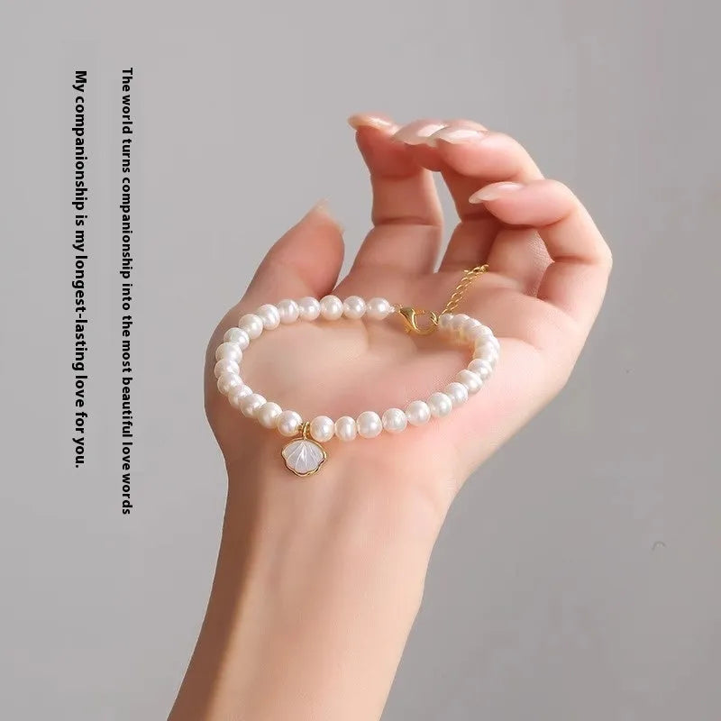 Women's freshwater pearl bracelet with a fan-shaped shell clasp on a wrist.