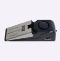 Black portable wedge door alarm with stainless steel cover placed against a hinged door.