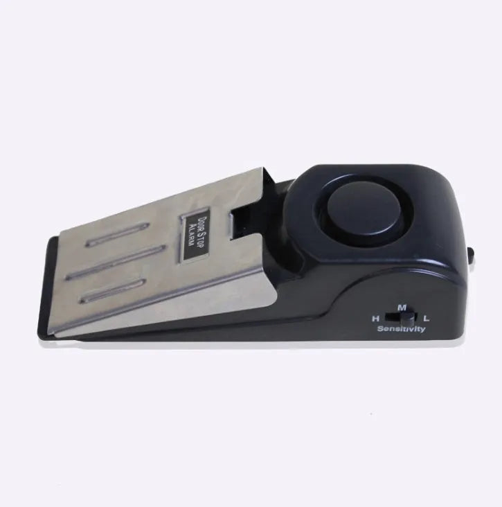Black portable wedge door alarm with stainless steel cover placed against a hinged door.