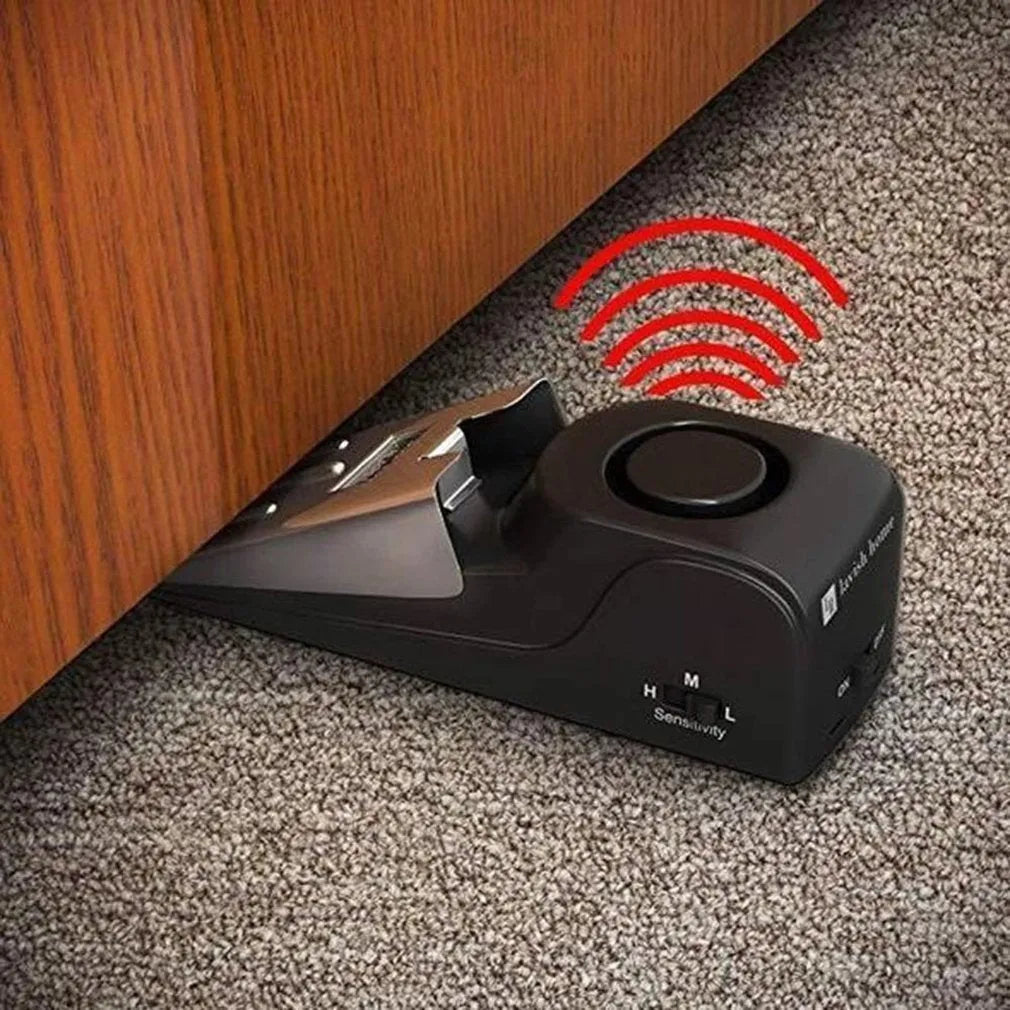 Black portable wedge door alarm with stainless steel cover placed against a hinged door.