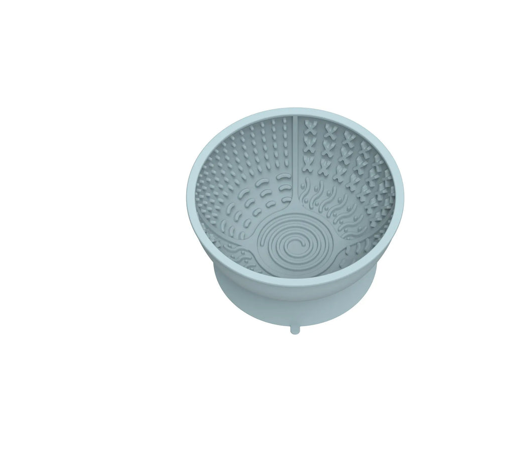 Cyan silicone dog bowl with textured slow-feed surface and a suction cup base on a kitchen floor.