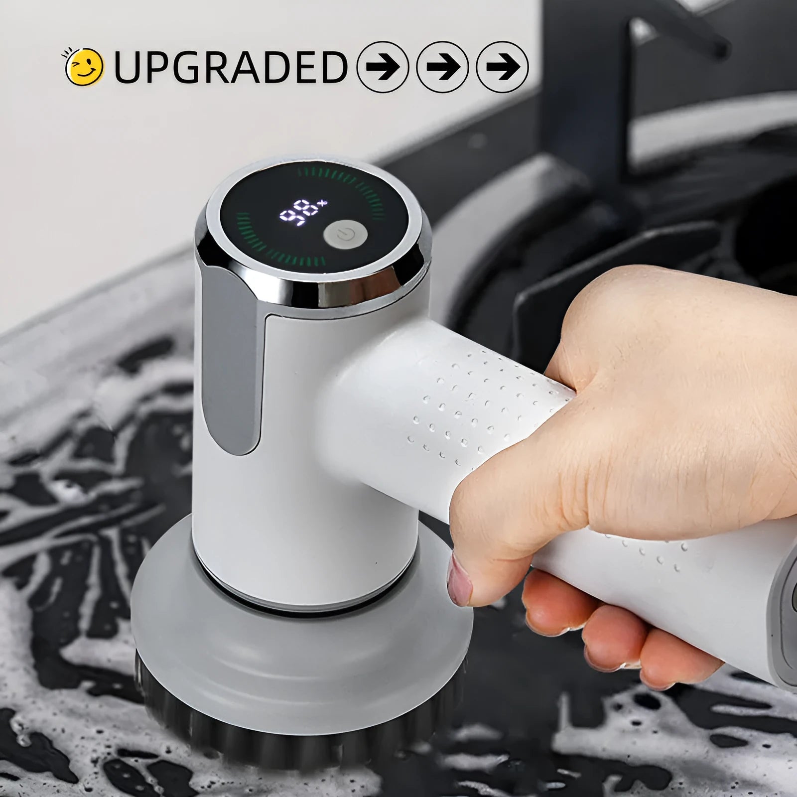 White cordless electric cleaning brush with interchangeable heads on a kitchen counter.