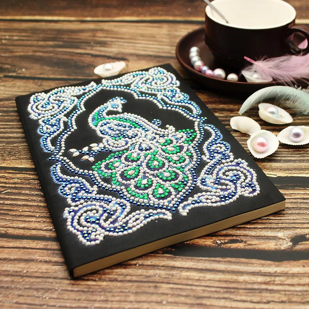 Black A5 hardcover Peacock Beauty journal open showing diamond painting canvas and organised drills in clear OPP bags.