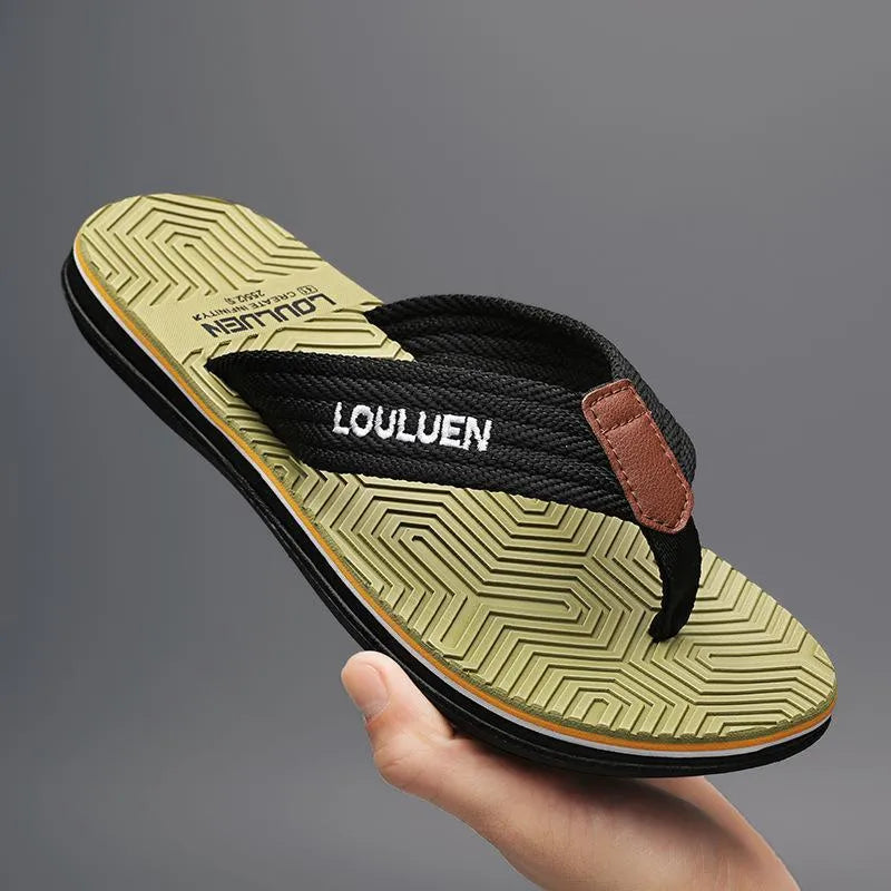 Men's black flip flops with open toe design and textured non-slip sole on a sandy beach.