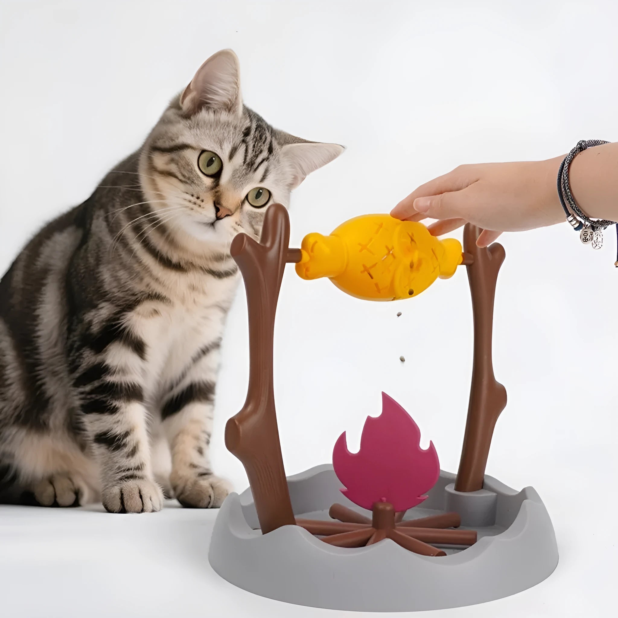 Barbecue-themed tumbling cat food feeder toy with treat dispenser, shown next to dry kibble.
