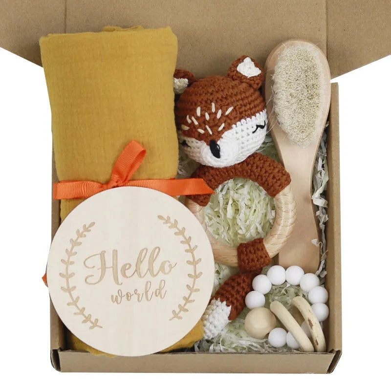 Baby teething toy gift set showing gauze blanket, wooden bell, gum teether, tire brush, and milestone on white background