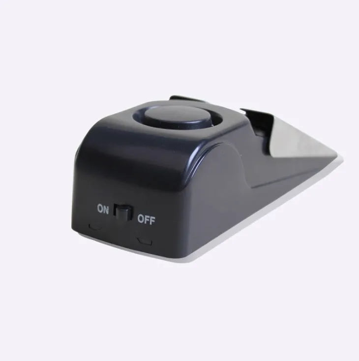 Black portable wedge door alarm with stainless steel cover placed against a hinged door.