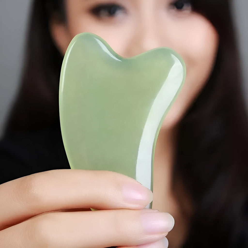 Flat natural jade gua sha stone for facial massage in green colour on white background