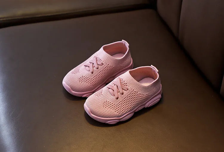 Children's white fabric lazy slip-on shoe with non-slip rubber sole on a wooden floor.