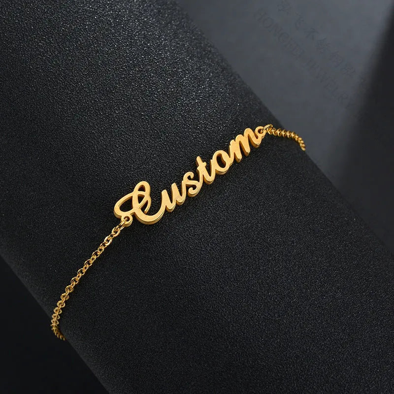 Gold titanium steel cable chain anklet with personalised name engraving on a sandy beach background