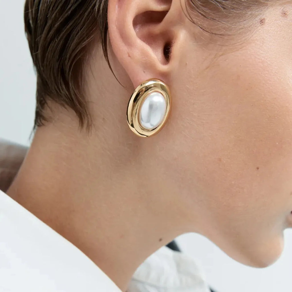 A pair of small stainless steel ear studs with a vintage-style pearl decoration on a silver-coloured base.