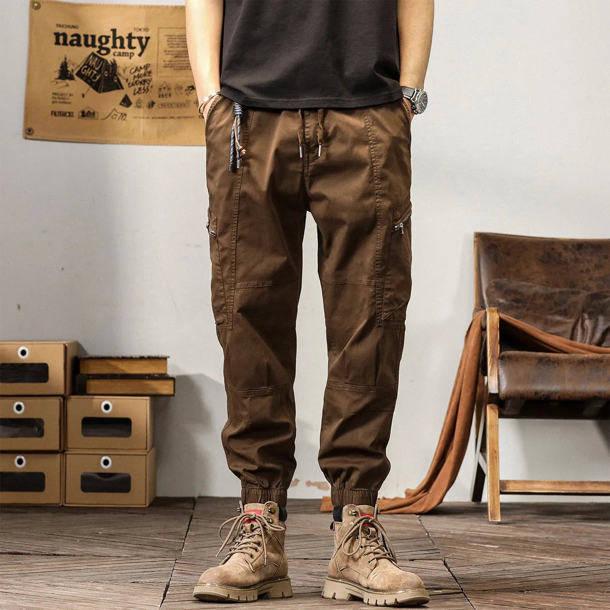 Man wearing khaki coloured cotton overalls with tapered legs and elasticated ankle bands.