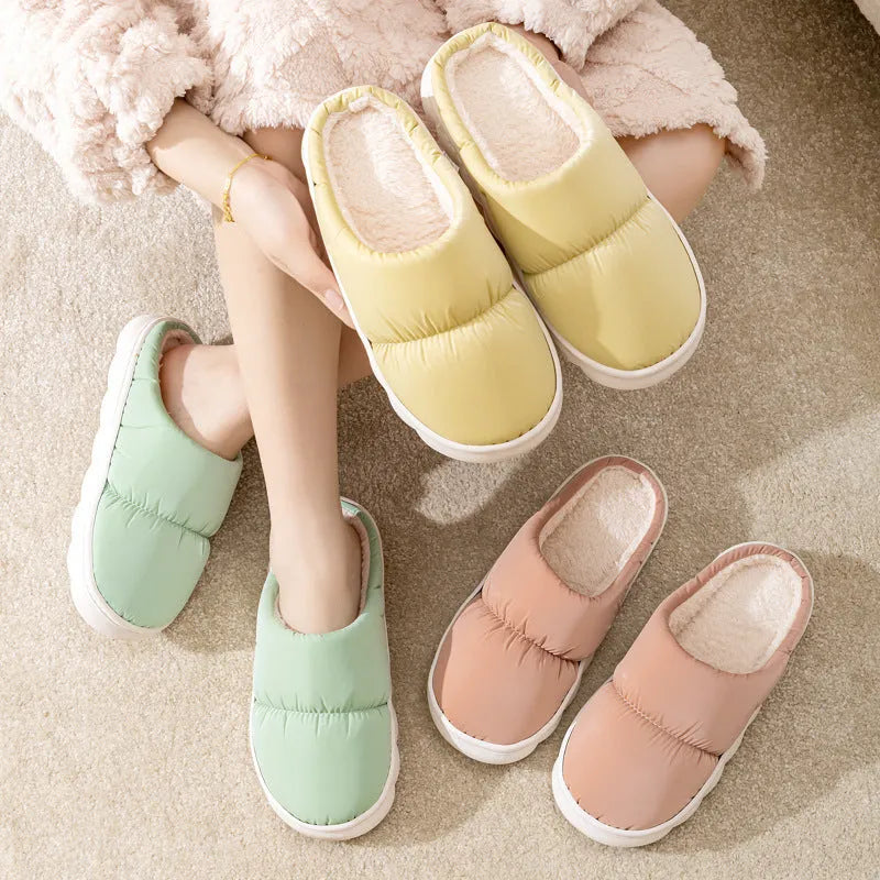 A pair of blue down cotton winter slippers with a thick rubber sole and plush lining on a wooden floor.