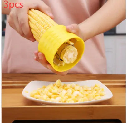 Yellow manual corn thresher kitchen tool with a corn-shaped plastic body and visible stainless steel gear.