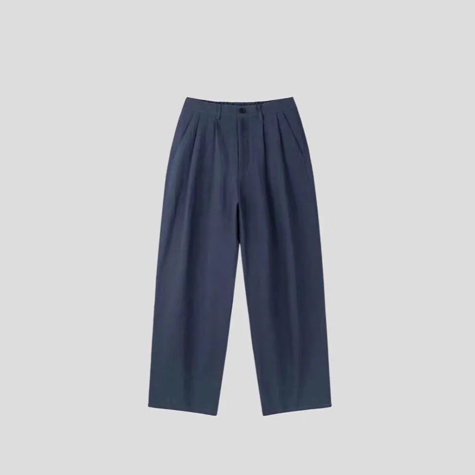 Men's apricot coloured loose-fit cotton linen suit trousers with a pencil leg on a neutral background.