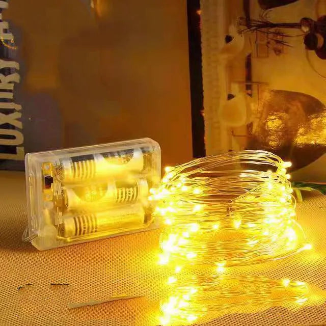Copper wire fairy lights wrapped around a jar, showing warm white LEDs and a small battery box on a wooden table.