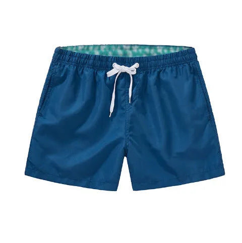 Men's straight-leg polyester surf shorts on a beach, showing colour options like black, fluorescent yellow, and navy blue.