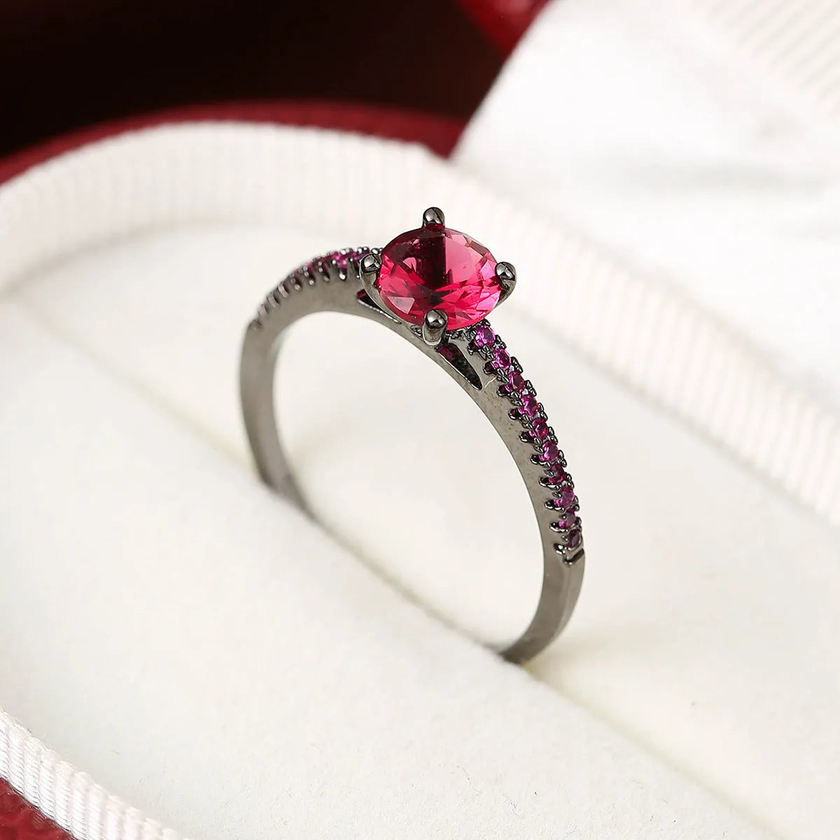 A hexagonal geometric ring with a zircon stone, shown in a gun black and rose red electroplated finish on a finger.