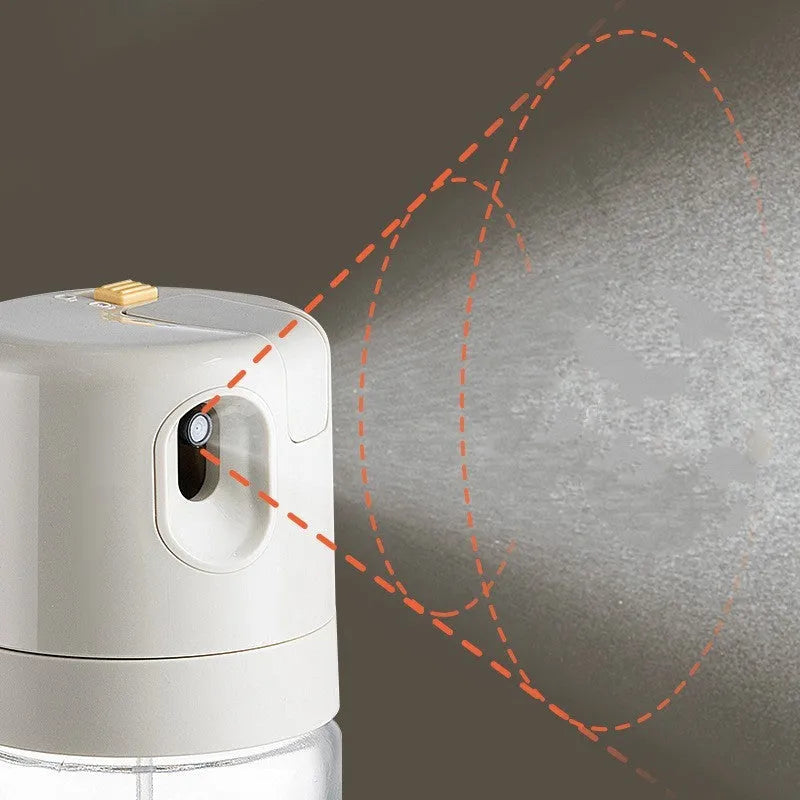 Warm grey glass oil sprayer bottle with a dual-mode cap switch, shown on a kitchen counter.