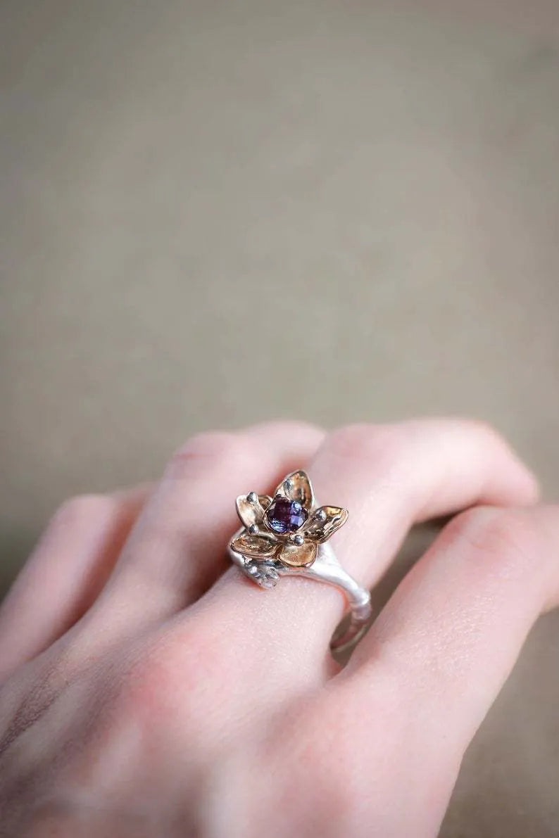 A silver two-tone floral ring with a geometric shape on a model's finger.