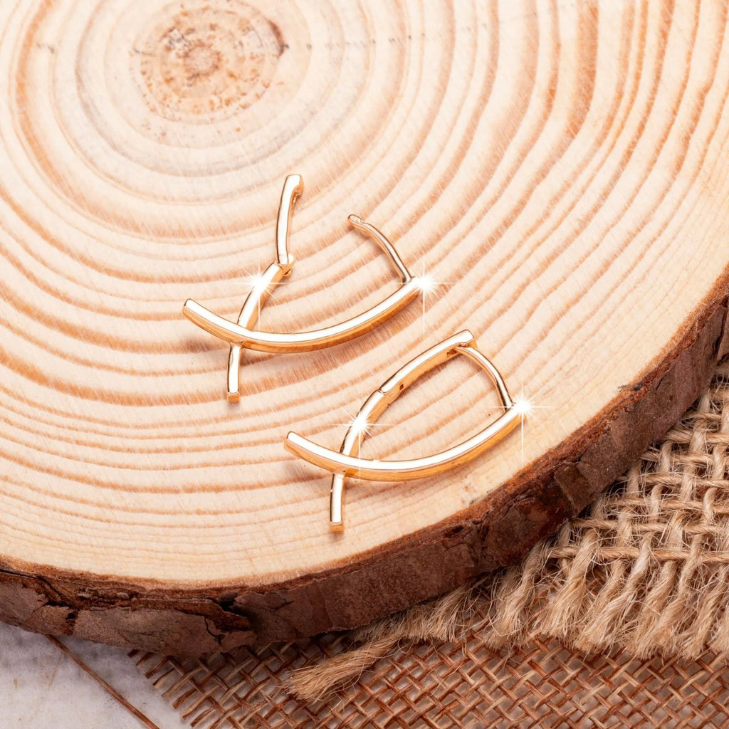 A pair of rose gold coloured cross-shaped earrings made from copper on a plain background.