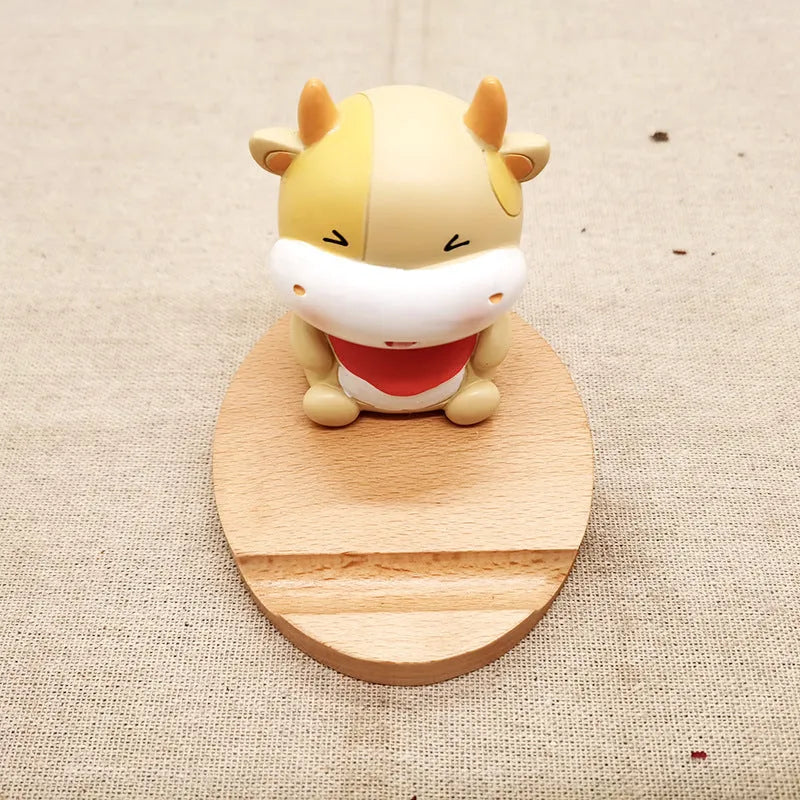 Solid beech wood mobile phone stand with a resin cow figurine and a slot for holding coins on a wooden desk.