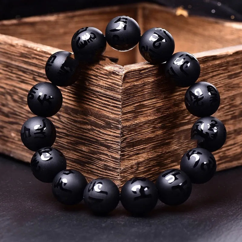Close-up of a frosted black agate bracelet with Sanskrit mantra engraving on each bead, showing matte stone texture.
