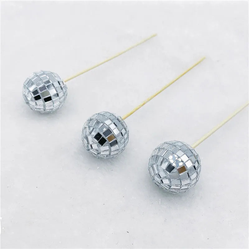Glass disco ball cake decoration on a wooden stick in various sizes on a cake.
