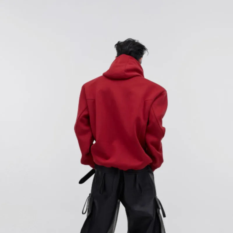 Man wearing a loose red hooded sweater with metallic 3D printing and structured shoulder pads.