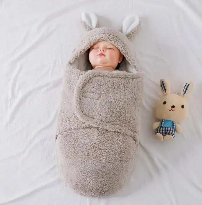 Baby wearing a grey adjustable fleece swaddle sleep sack with velcro wings