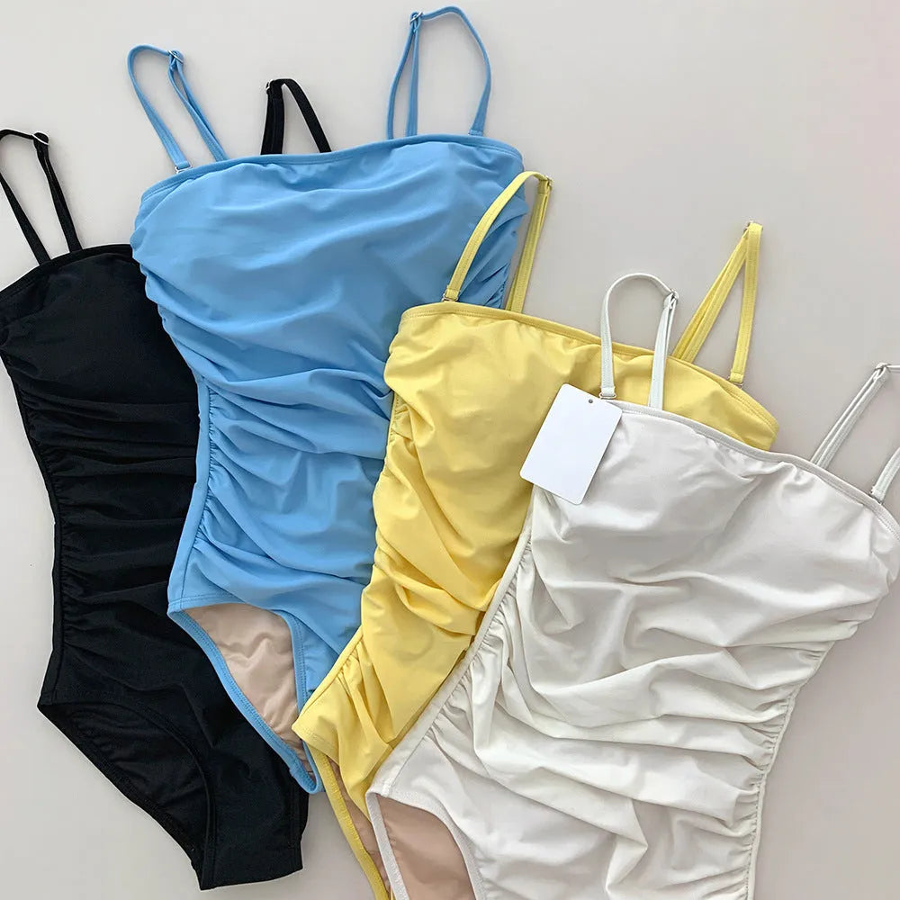 Blue sling style one-piece swimsuit with belly pleats and slim fit on model.