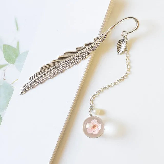 Close-up of a metal bookmark with a dried dandelion flower sealed inside, showing its 12cm length and slim profile.