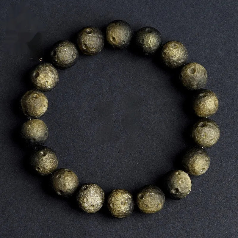 Obsidian crater ball bracelet on a wrist, showing ground stone texture and bead size.