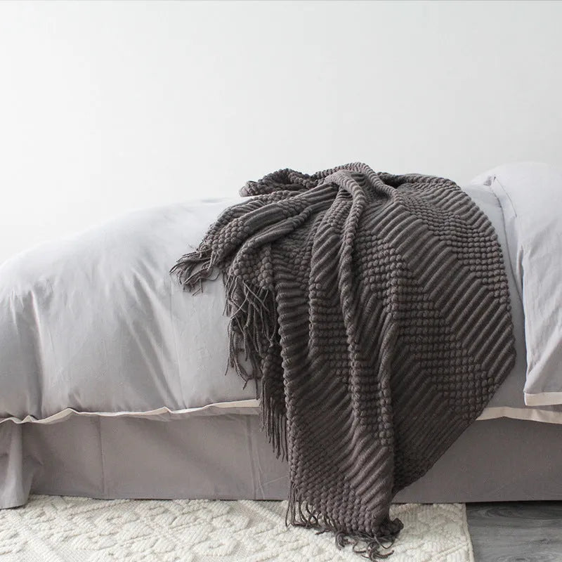 Small dark grey polyester nap blanket folded on a sofa, showing its 127x170cm size.