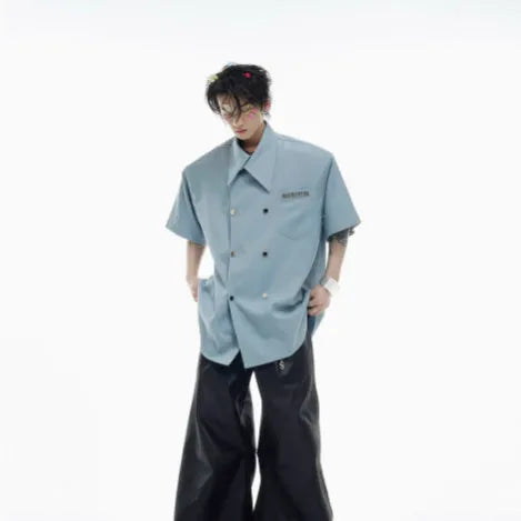 A man wearing a loose-fitting black short-sleeved casual shirt with spliced detailing and metal buttons.