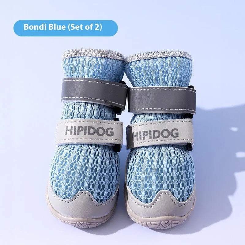 Pair of blue and green breathable mesh dog shoes with thick rubber soles and hook-and-loop straps on a wooden floor.