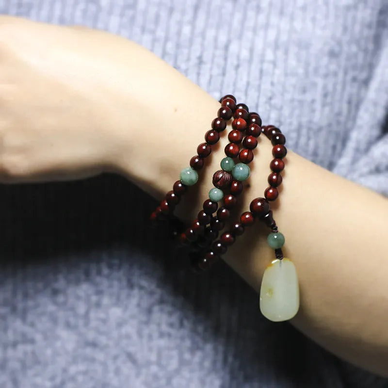 A wooden beaded bracelet with a carved green Hotian jade pendant on a natural background.