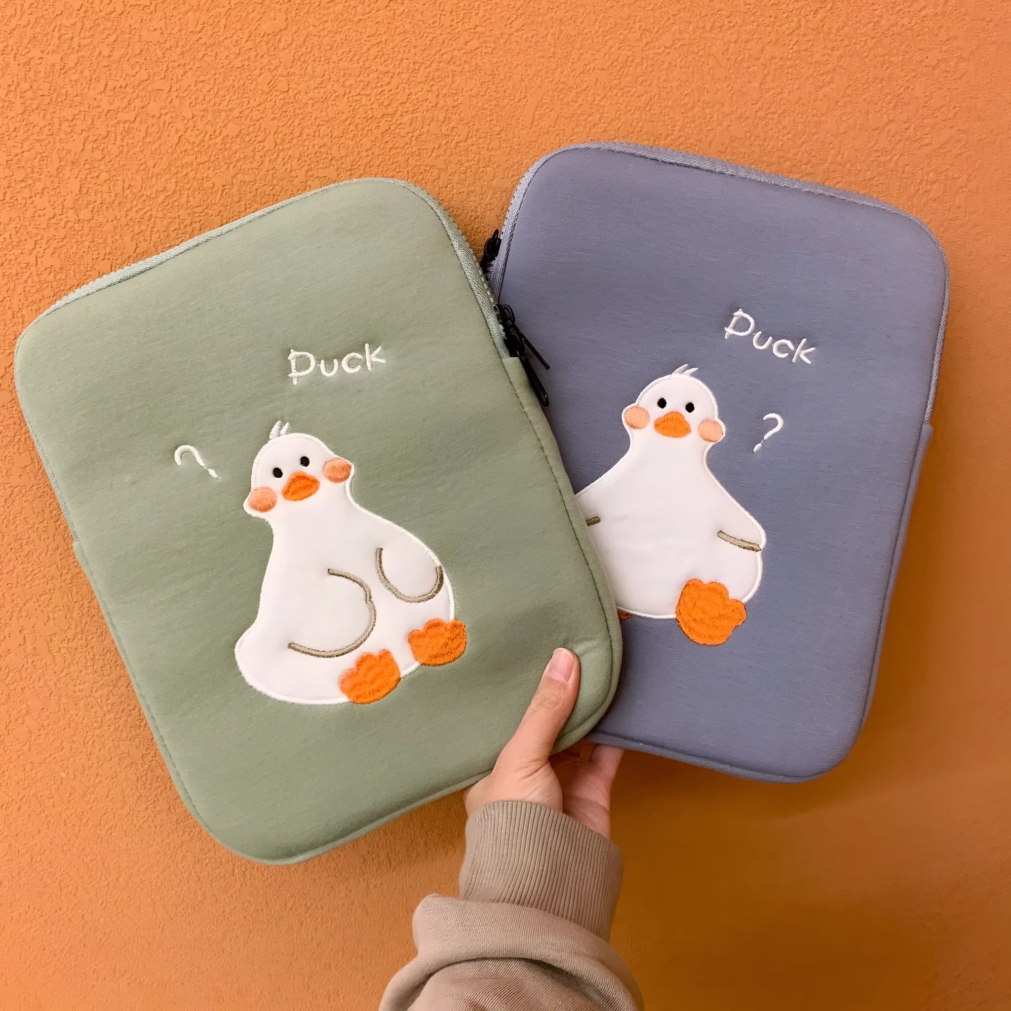 Blue cotton tablet case with embroidered cartoon duck design, showing zipper closure and protective frame.