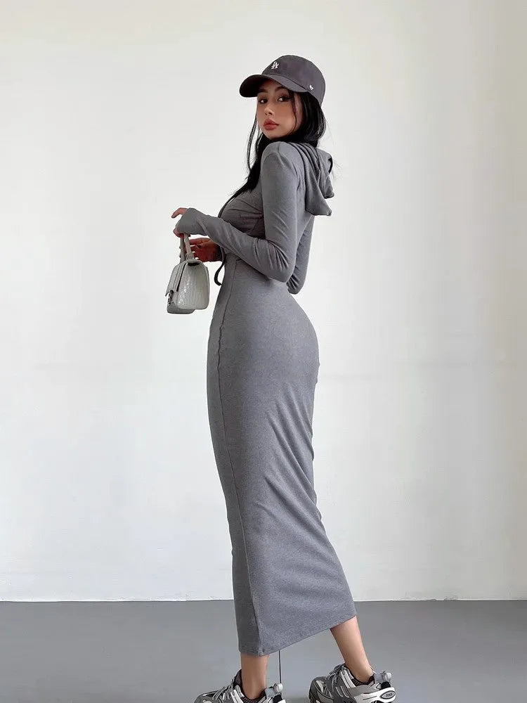 A woman modelling a grey hooded long-sleeve sheath dress with a high waist and over-the-knee length.