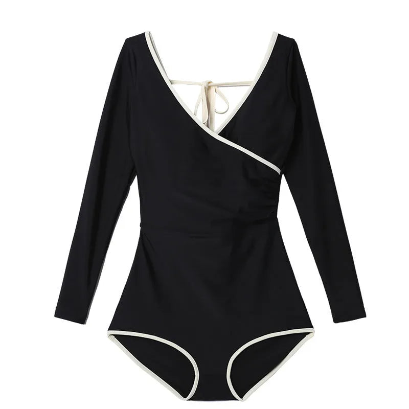 Women’s long sleeve conservative one-piece swimsuit in solid black with white edge trim on a model.