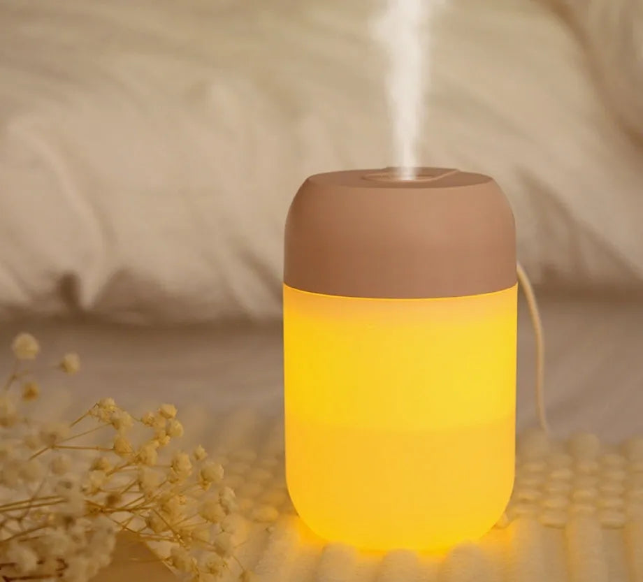 Small white cylindrical USB mini humidifier on a surface with its charging cable.