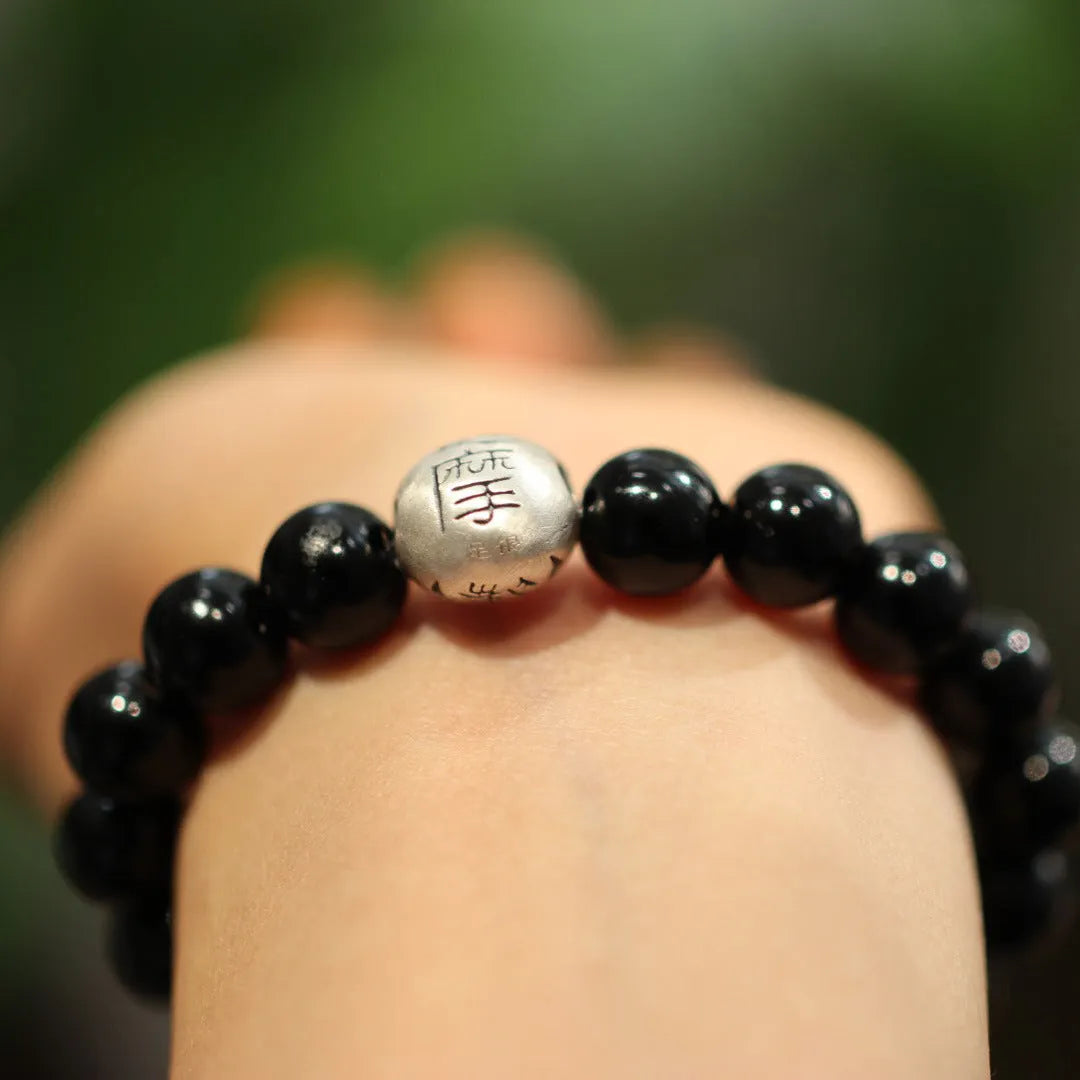 Close-up of a women's bracelet with large black agate beads and a sterling silver clasp on a wrist.