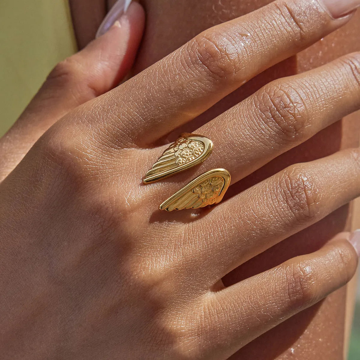 Wings design adjustable stainless steel ring with electroplated colour finish on a plain background.