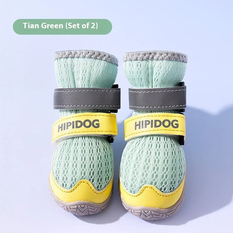 Pair of blue and green breathable mesh dog shoes with thick rubber soles and hook-and-loop straps on a wooden floor.