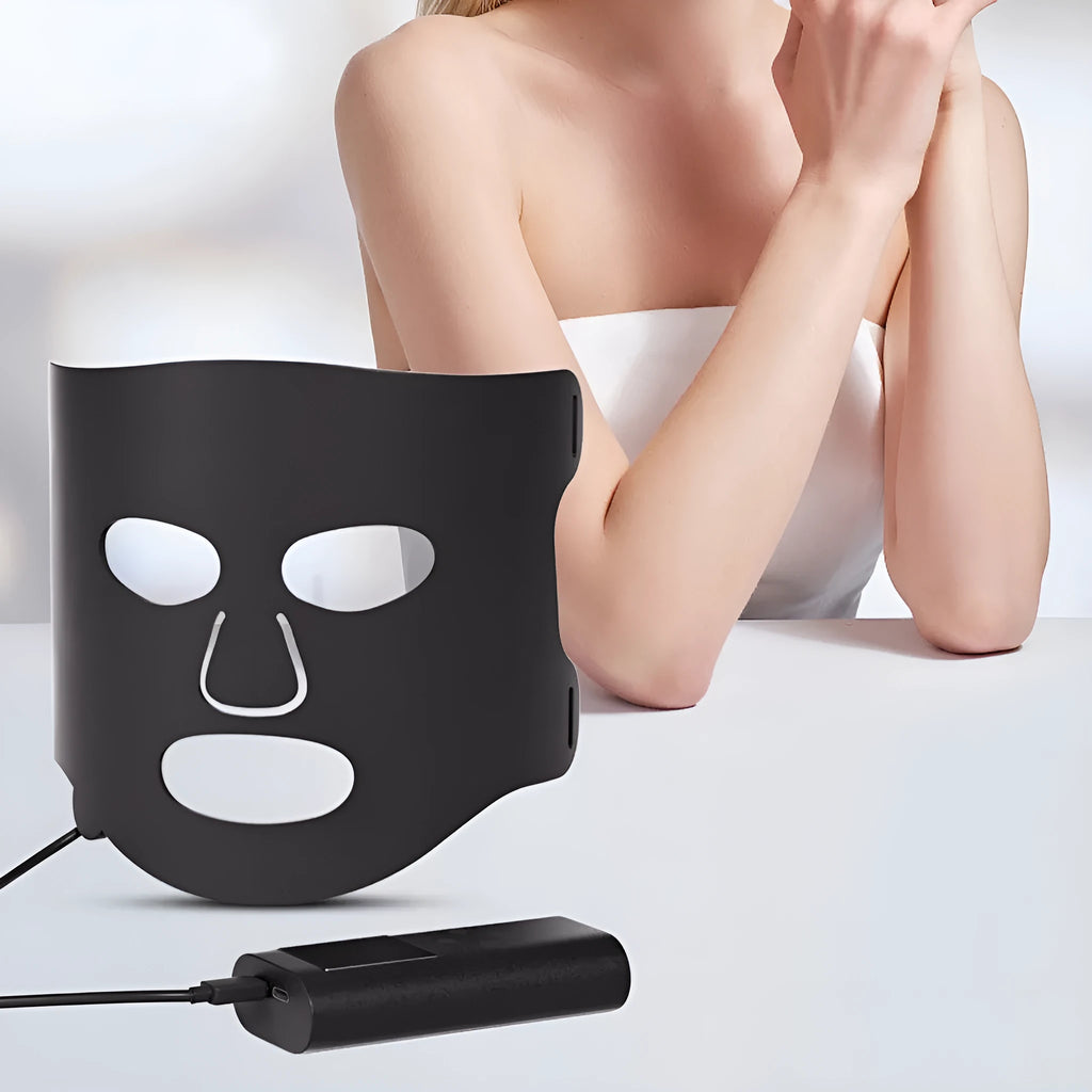 Black and white LED phototherapy face mask with controller on a strap for home skincare use.