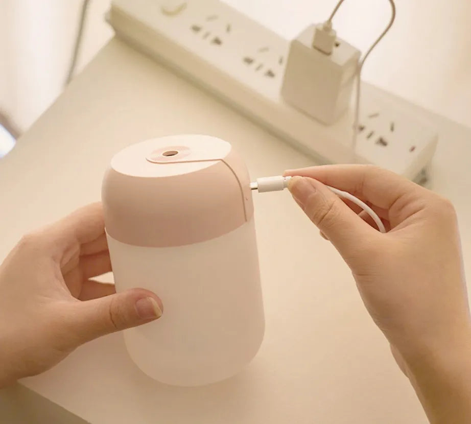 Small white cylindrical USB mini humidifier on a surface with its charging cable.