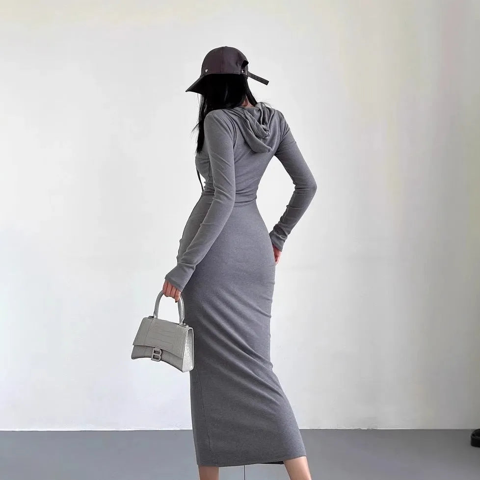 A woman modelling a grey hooded long-sleeve sheath dress with a high waist and over-the-knee length.