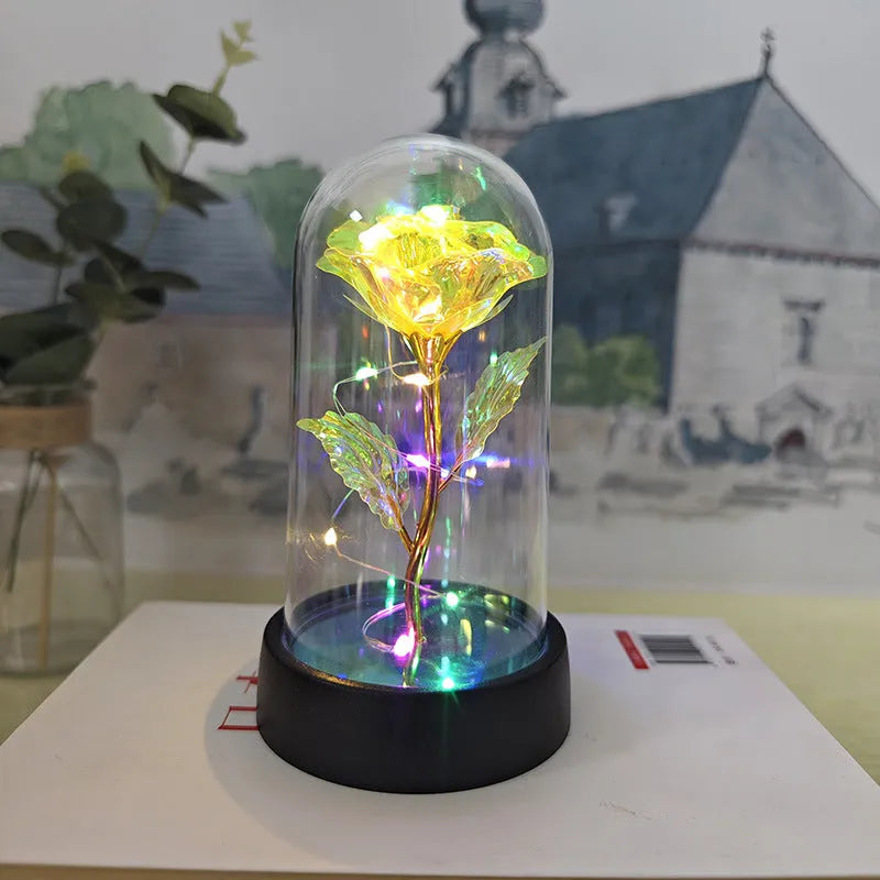 Small glass cover night lamp with plastic flowers, showing coloured LED light options on a black base.